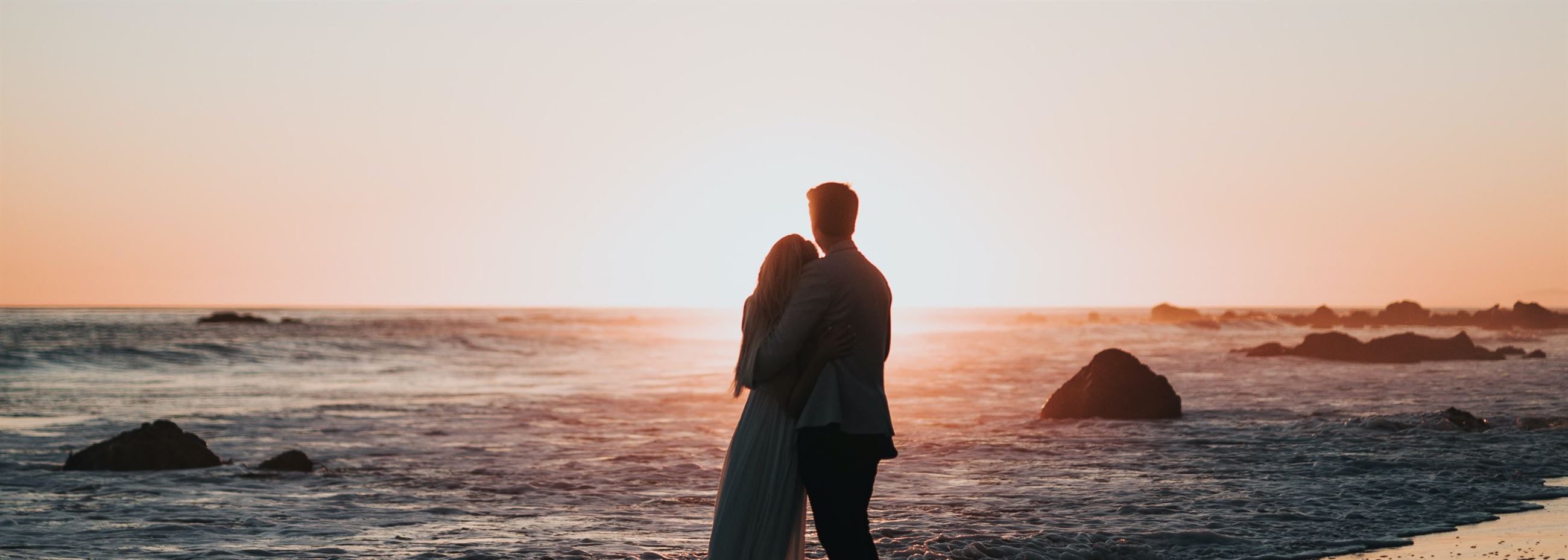 Сouple wearing a white gown and a black suit on the beach